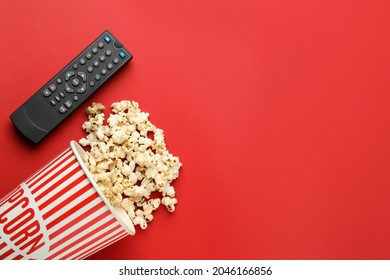 Remote control and cup of popcorn on red background, flat lay. Space for text