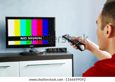 Remote control in hand in front of TV. Couch potato. No signal screen banner.