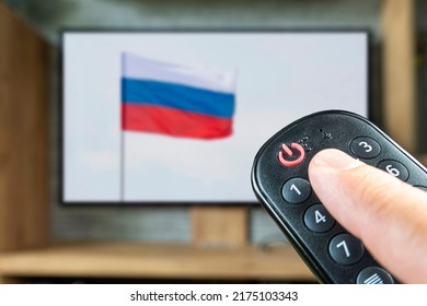 Remote control in a man's hand on the background of a TV and a Russian flag. The concept of disconnecting Russian channels in Europe and the USA. Blocking of Russian TV broadcasting. - Shutterstock ID 2175103343