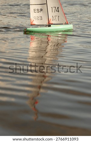Remote control model boats moving across a calm lake water surface outdoors.