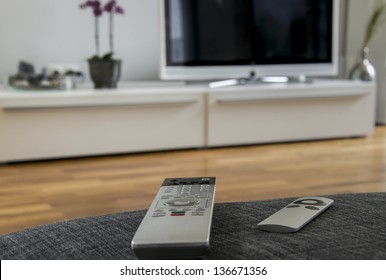 a remote controller is lying on the grey sofa with the home theater in the background
