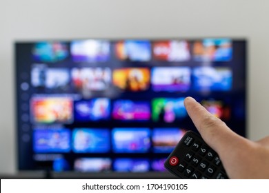 Remote Controller And Tv Blurred In Background. Video Streaming Service Catalogue In Grid Blurred On Smart TV. 