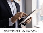 Remote data access. Close up cropped shot male business specialist wear formal suit stand by office window work online on digital tablet. Professional interaction browsing news reading report concept