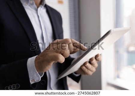 Remote data access. Close up cropped shot male business specialist wear formal suit stand by office window work online on digital tablet. Professional interaction browsing news reading report concept