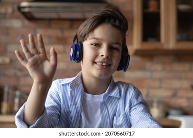 Remote Education For Children. Screen View Portrait Of Junior School Age Boy In Wireless Headphones Join Online Class Wave Hand Greet Tutor Teacher. Smiling Tween Kid Look At Web Camera Make Videocall