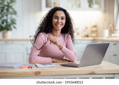 Remote Entrepreneurship. Portrait Of Happy Millennial Woman Sitting At Table With Laptop In Kitchen, Smiling Young Lady Holding Glasses And Looking At Camera, Enjoying Working From Home, Free Space