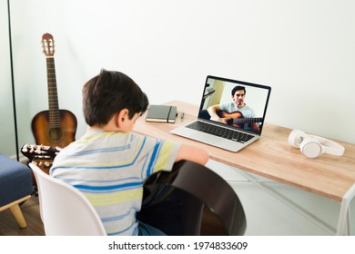 Remote Guitar Lessons At Home. Rear View Of An Elementary Boy Playing The Acoustic Guitar To Show The Music Teacher His New Song On A Video Call 