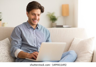 Remote Job. Man Working On Laptop Sitting On Sofa At Home. Empty Space For Text