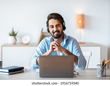 Remote Job Opportunities. Portrait Of Smiling Arab Man Hotline Manager In Headset Posing At Workplace, Eastern Guy Sitting At Desk With Laptop At Home Office And Looking At Camera, Copy Space