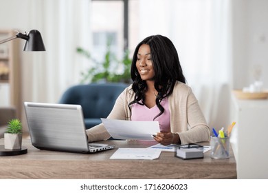 Remote Job, Technology And People Concept - Happy Smiling African American Young Woman With Laptop Computer And Papers Working At Home Office