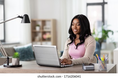 Remote Job, Technology And People Concept - Happy Smiling African American Young Woman With Laptop Computer Working At Home Office