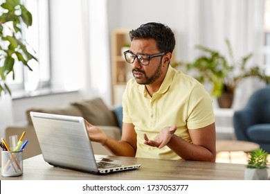 remote job, technology and people concept - sad young indian man in glasses with laptop computer working at home office
