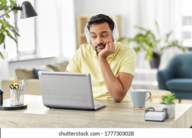 Remote Job, Technology And People Concept - Bored Young Indian Man In Headphones With Laptop Computer Working At Home Office