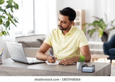 remote job, technology and people concept - young indian man with notebook and laptop computer at home office