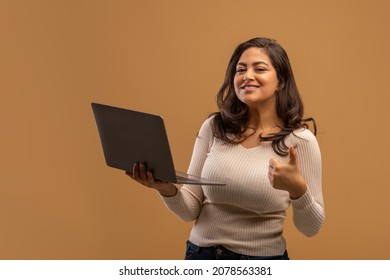 Remote Jobs For Students. Happy Arab Woman Holding Laptop And Showing Thumb Up, Brown Studio Background, Copy Space. Positive Lady Using Notebook, Shopping Online Or Websurfing