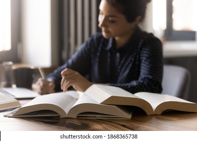 Remote Learning. Diligent Millennial Mixed Race Female Student Prepare For Exam At Home. Confident Indian Woman Write Up Notes Thesis For Research Report Essay. Focus On Opened Paper Books On Table