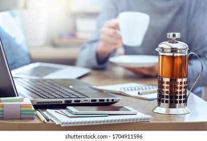 Remote learning or work. Closeup french press of tea on home table with a laptop in the morning against the background of a working man.  