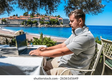 Remote Tech Work by the Sea: Man Using Laptop at Cafe in Sveti Stefan, Montenegro — Digital Nomad Lifestyle, Cloud Computing, Online Business, Global Connectivity
