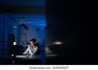 Remote view of serious young business man remote working overtime, learning online late at night in in dark room with neon light using desktop computer at workplace. Concept overwork and deadline. - Powered by Shutterstock