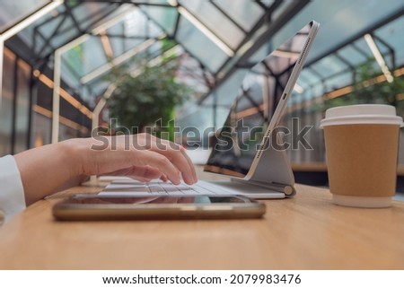 Remote work or freelance, modern opportunities for a mobile lifestyle. Women's hands are typing on keyboard of tablet computer, close-up side view, public space hall on background, low depth of field.