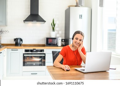 Remote Work From Home. Call-centre Worker. Portrait Of A Young Business Woman Working On Laptop Computer, Talking Online Using A Headset While Sitting On The Kitchen At Home