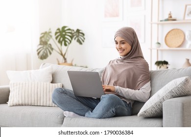 Remote Work For Muslim Women. Happy Arab Girl Working With Laptop At Home, Using Computer While Sitting On Couch In Living Room