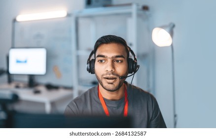 Remote work online technical support concept. Portrait young adult indian man wearing headset typing keyboard working in office. It support business customer service technology.