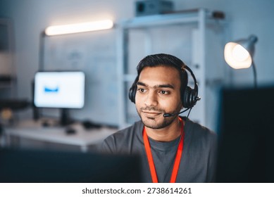 Remote work online technical support concept. Portrait young adult indian man wearing headset typing keyboard working in office. It support business customer service technology.