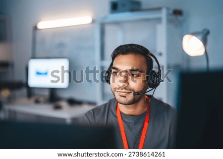 Remote work online technical support concept. Portrait young adult indian man wearing headset typing keyboard working in office. It support business customer service technology.