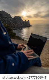 Remote work sunset laptop worker using keyboard outdoors on rugged cliff overlooking ocean