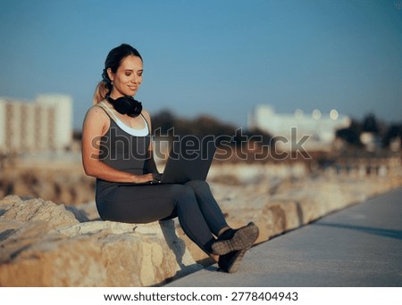 Remote Worker using Laptop on Beach Concrete Breakwater. Digital nomad woman working outdoors seaside wearing activewear and headphones near sea waves