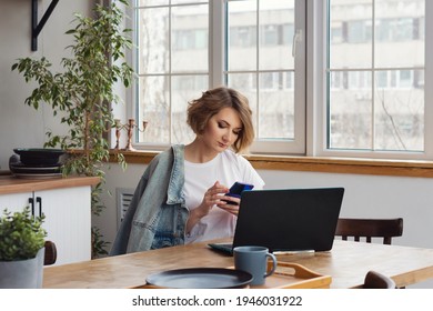 Remote Working From Home. Girl Freelancer Workplace In Kitchen With Laptop, Mug Of Tea Or Coffee. Concept Distance Learning, Self Isolation, Female Small Business, Shopping Online. Lifestyle Moment.