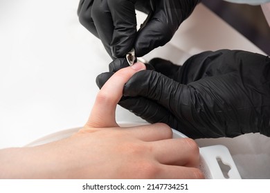 Removal of cuticle with nail clippers. Gloved hands of a skilled manicurist cutting cuticles with metal tweezers, close-up. Hands during a manicure care session in a spa salon. Nail care