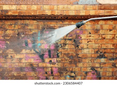 Removal of graffiti paint on a facade. Worker cleaning a dirty brick facade with a pressurized water jet in the integral reform of a house. Municipal facade cleaning service