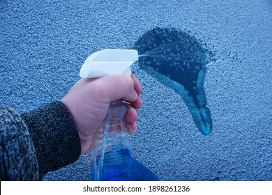 Removal ice from automobile windshield. Hand with liquid spray for car window defrost in winter season. 