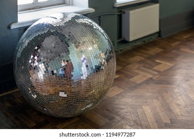 Removed old disco ball on hardwood wooden floor. Needless nightclub accessory from past. End of party concept