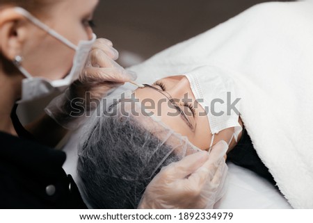 Removing anesthetic cream from the eyebrows before the permanent makeup procedure. Master and client in medical masks and gloves. Permanent makeup eyebrows conturing. New reality in beauty world