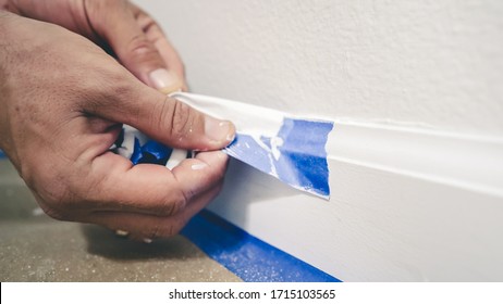 Entfernen des Maskierungsbandes aus der Formgebung. Ein Maler zieht das blaue Maler-Band von der Wand, um ein sauberes Randbaseboard zu enthüllen.