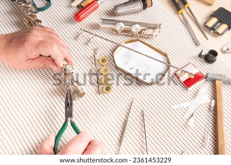 removing a screw from a flute in the foreground. two hands with pliers on a table in a lutherie workshop.