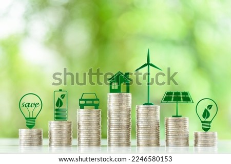 Renewable or clean energy generation prices and costs, financial concept : Green eco-friendly symbols atop coin stacks e.g. energy efficient light bulb, a battery, a solar cell panel, a wind turbine.