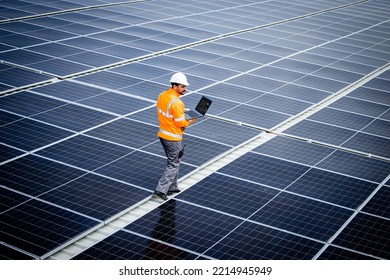 Renewable energy engineer walking through large solar power plant and checking electricity production on his laptop computer. Sustainable energy source and eco friendly technologies. - Shutterstock ID 2214945949