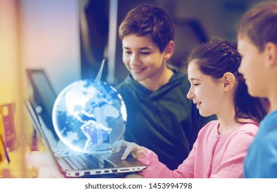 renewable energy, science and technology concept - group of happy children with laptop computer, earth planet hologram and wind turbine model at school - Powered by Shutterstock