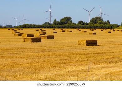 Renewable energy wind turbines behind a freshly harvested agricultural field with square hay bales