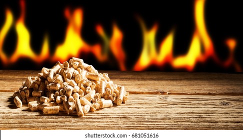 Renewable or sustainable energy concept with a row of burning flames behind a heap of natural wood pellets in a panorama view with copy space