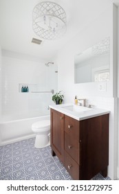 A Renovated Bathroom With A Blue And White Mosaic Tile Floor, Wood Vanity Cabinet, White Chandelier, And A Subway Tile Shower.