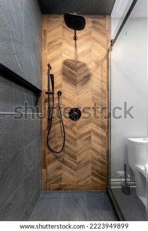 Renovated modern bathroom with walk-in shower. Dark (Black Grey) tile with herringbone wood pattern design tiled wall with niche.