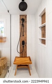 Renovated modern bathroom. Whitish tile accent wall with wood-colored tile niche. Black shower fixtures and Teak wood bench. - Shutterstock ID 2223949961