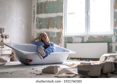 Renovation apartment. Creative story young happy woman sits in bathtub in the middle of the room. Empty walls, repairs house with their own hands. - Shutterstock ID 1921760183