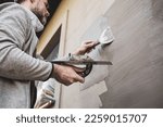 Renovation of the building facade - construction industry. Worker man (plasterer) plastering exterior walls of a house.
