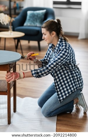 renovation, diy and home improvement concept - woman in gloves with paint brush painting old wooden table to grey color
